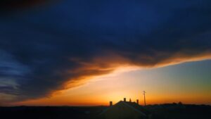 Ominous heavy clouds over dramatic April sunset with wide skyline, a small house silhouetted in the foreground