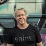 Australian Producer Damo Cox in black tee standing by graffiti wall
