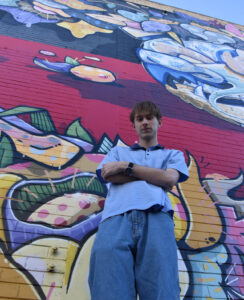 Sammy Smooth standing in front of graffiti wall 